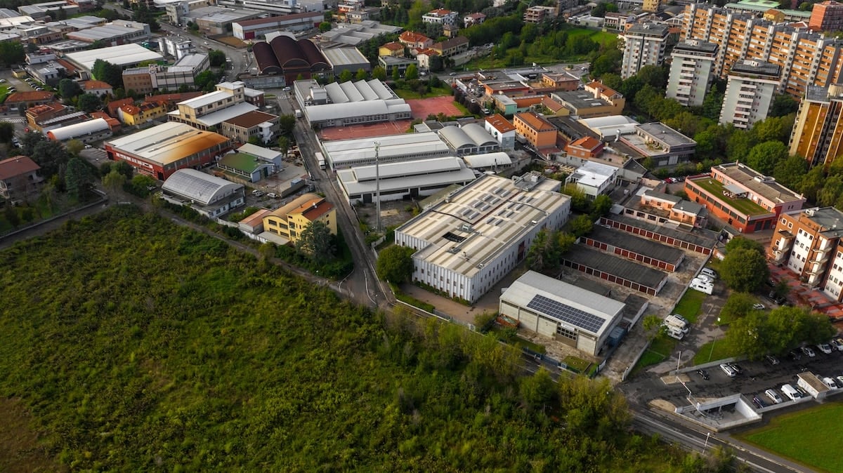 High-angle urban view of industrial buildings, orange apartment blocks, and a green field. "CCSI" is on a roof.