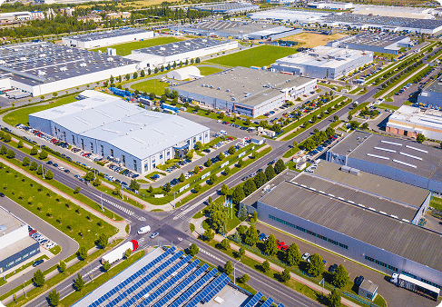 High-angle aerial view of a sprawling industrial park featuring modern warehouses, busy roads, and solar panels.